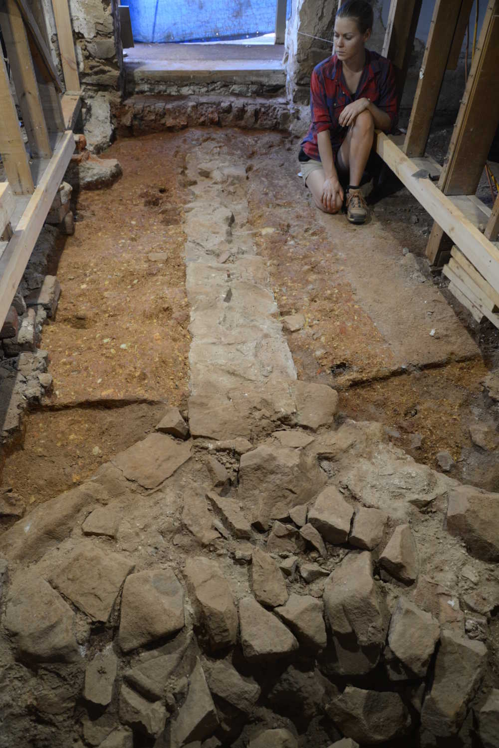 Archaeologist Lauren Gryctko inspects the foundation for a stone partition that divided a 17-by-34 foot stone dwelling on Mulberry Row into two rooms. Each room was heated by a corner fireplace supported by the triangular stone foundation in the foreground. The building was built  between 1776 and 1778 to house free white workmen that Jefferson hired to build Monticello I . It later housed  enslaved domestics, then free workmen again, and finally may have been used as a textile shop before Jefferson’s death in 1826. Image courtesy of Monticello.