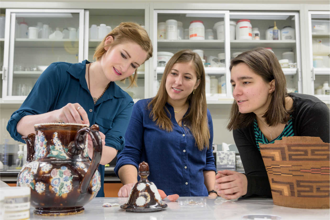 Leah Bright, Samantha Owens, and Madeline Corona (from left to right), NEH Fellows in the Winterthur/University of Delaware Program in Art Conservation, examine a few of their conservation projects including a 19th-century English earthenware teapot as part of their second year of study in object conservation.  Image courtesy of Evan Krape, University of Delaware.