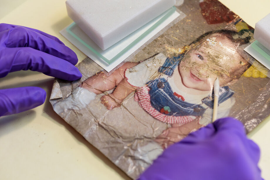 Jacklyn Chi, a first-year Master’s student in the Winterthur/University of Delaware Program in Art Conservation removes embedded dirt and grime using a dry cotton swab from a family photograph salvaged from the Wimberley, Texas floods. Image courtesy of Evan Krape, the University of Delaware.