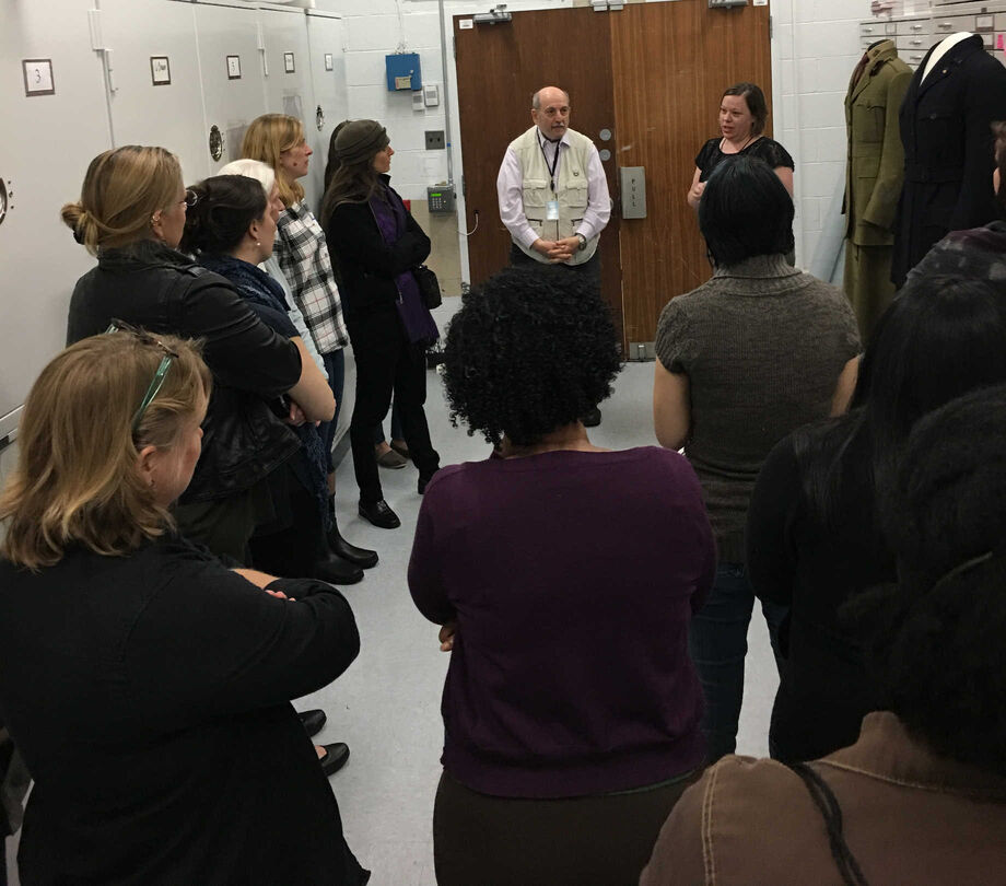 Participants crowd around century-old women’s military uniforms in a storage facility at the Smithsonian National Museum of American History. Image courtesy of the University of Maryland, College Park.